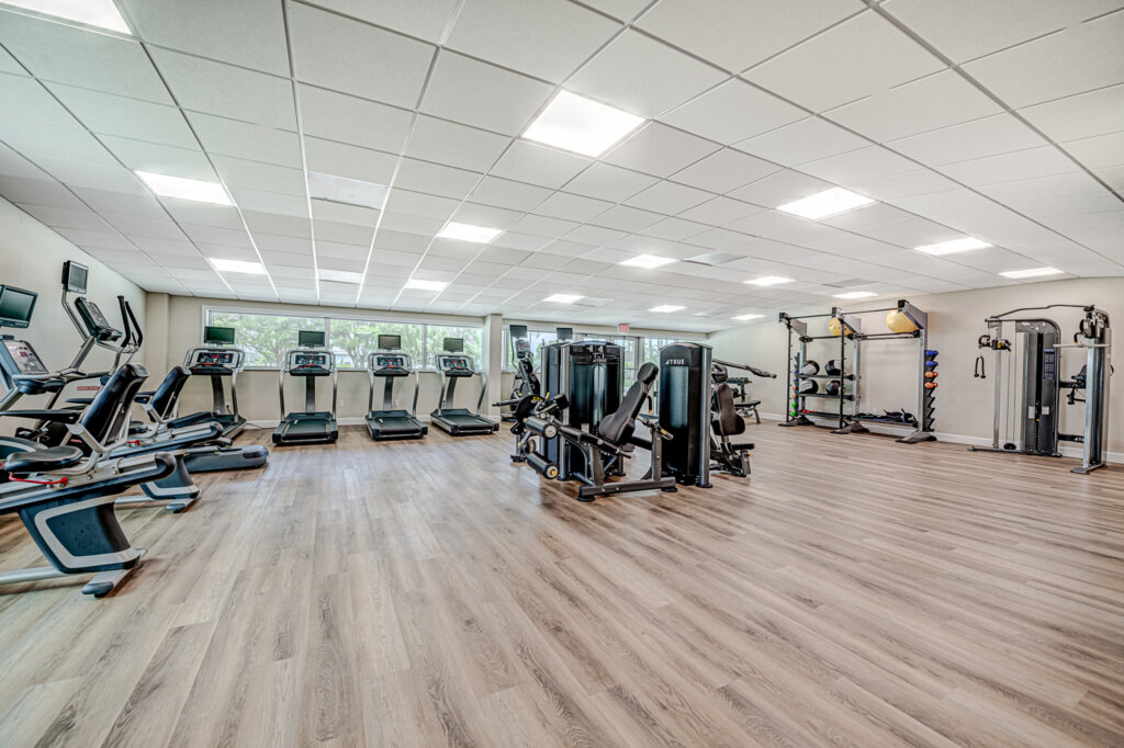 Bonita Terra Fitness room features wooden floors, cardio exercise and weightlifting machines under white lights
