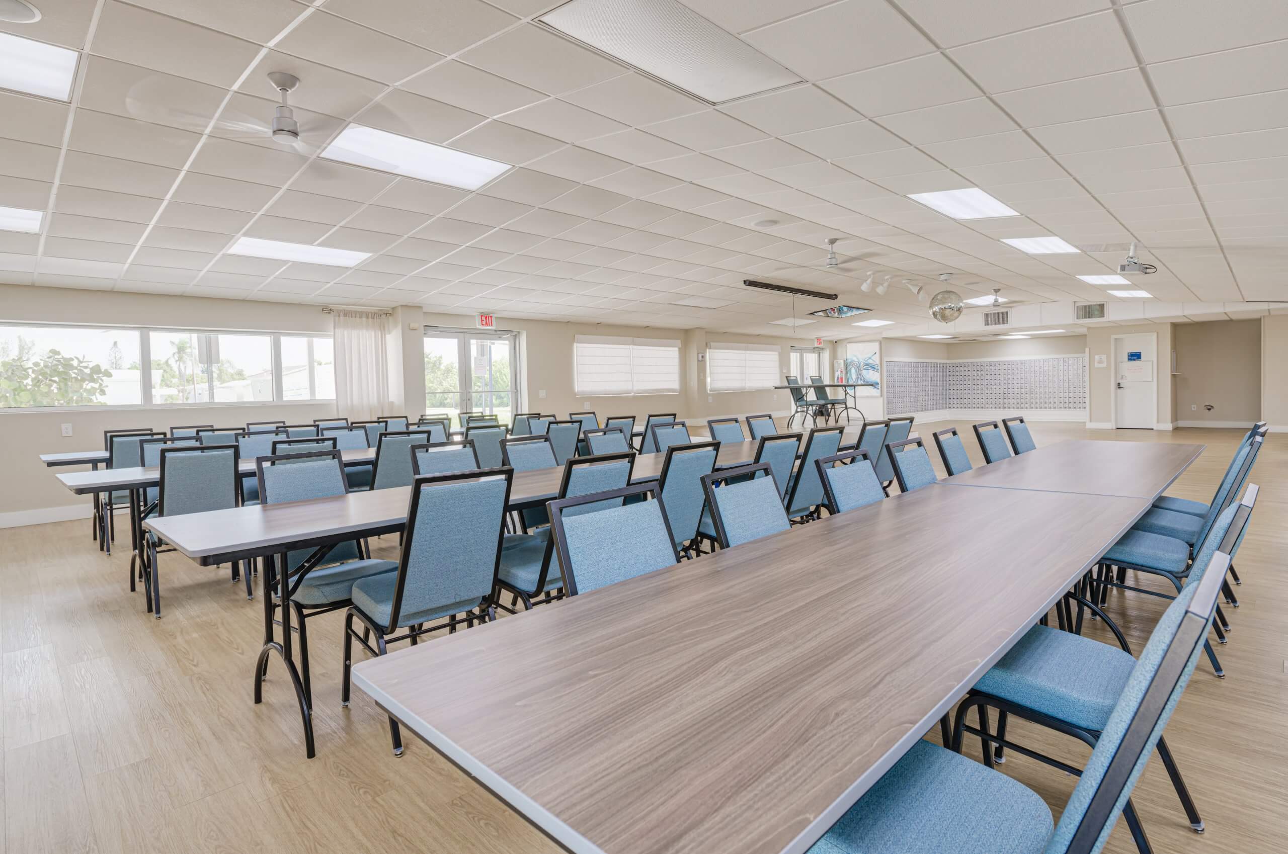 Another view of a bright community room with multiple tables and chairs, and a mailbox area in the back in Bonita Springs, FL
