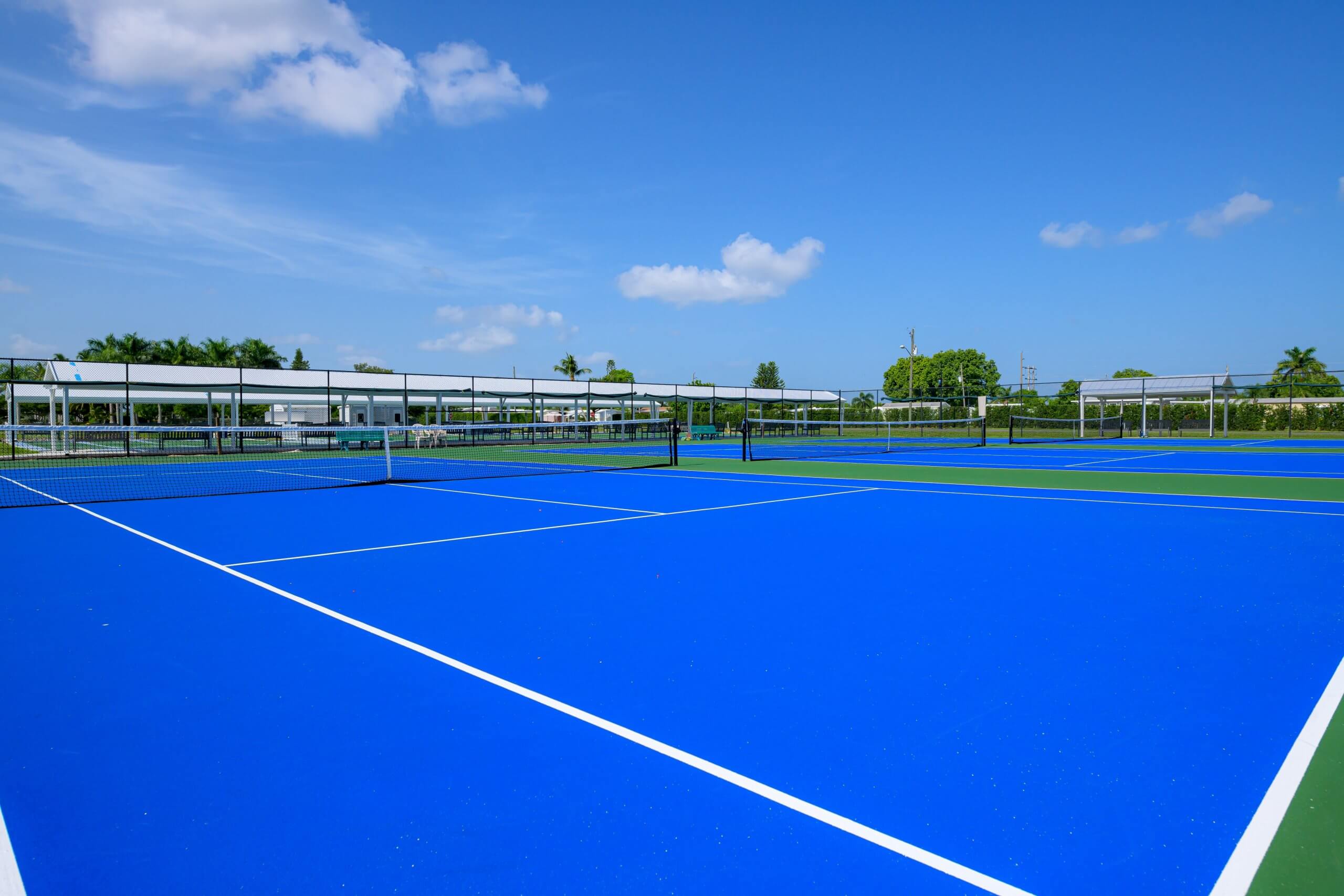 Bright blue tennis courts under a clear blue sky, surrounded by fencing and greenery in Bonita Springs, FL