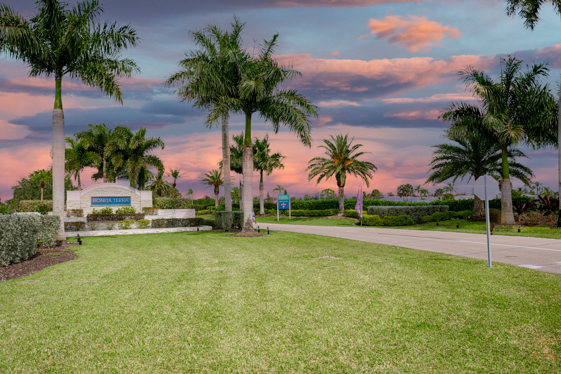 Entrance to Bonita Terra community with palm trees, landscaped greenery, and a sunset sky in Bonita Springs, FL