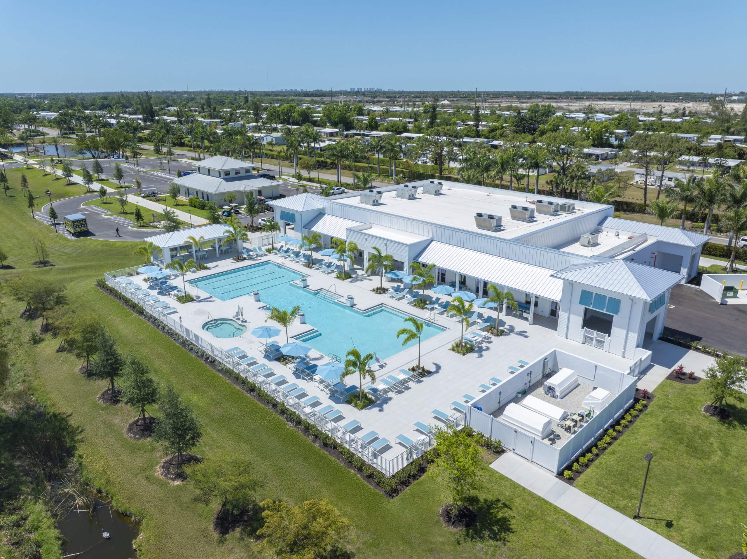 Aerial view of a modern clubhouse with a large outdoor pool, spa, lounge chairs, and surrounding greenery in Bonita Springs, FL