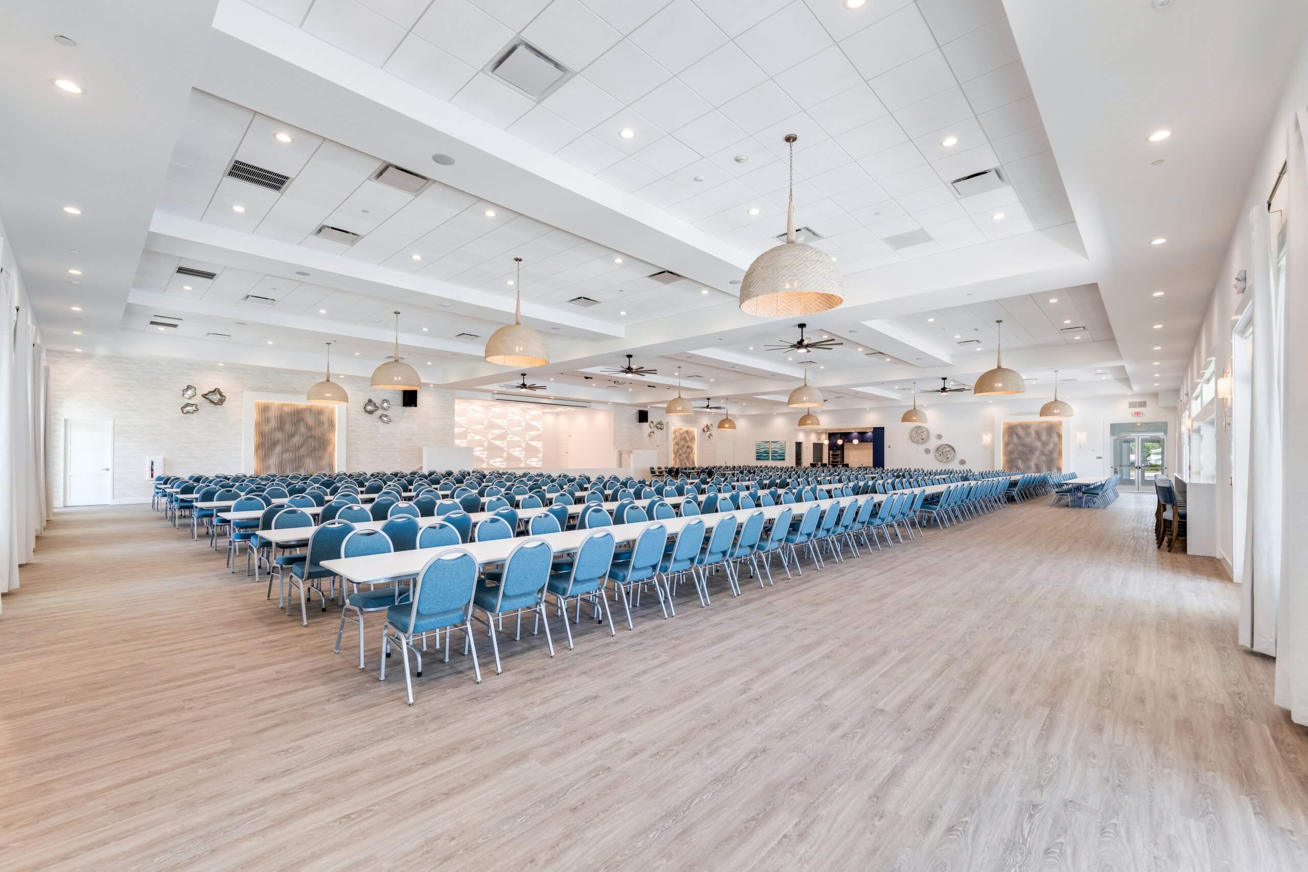 Spacious event hall with rows of blue chairs and long tables, ceiling fans, and pendant lighting in Bonita Springs, FL