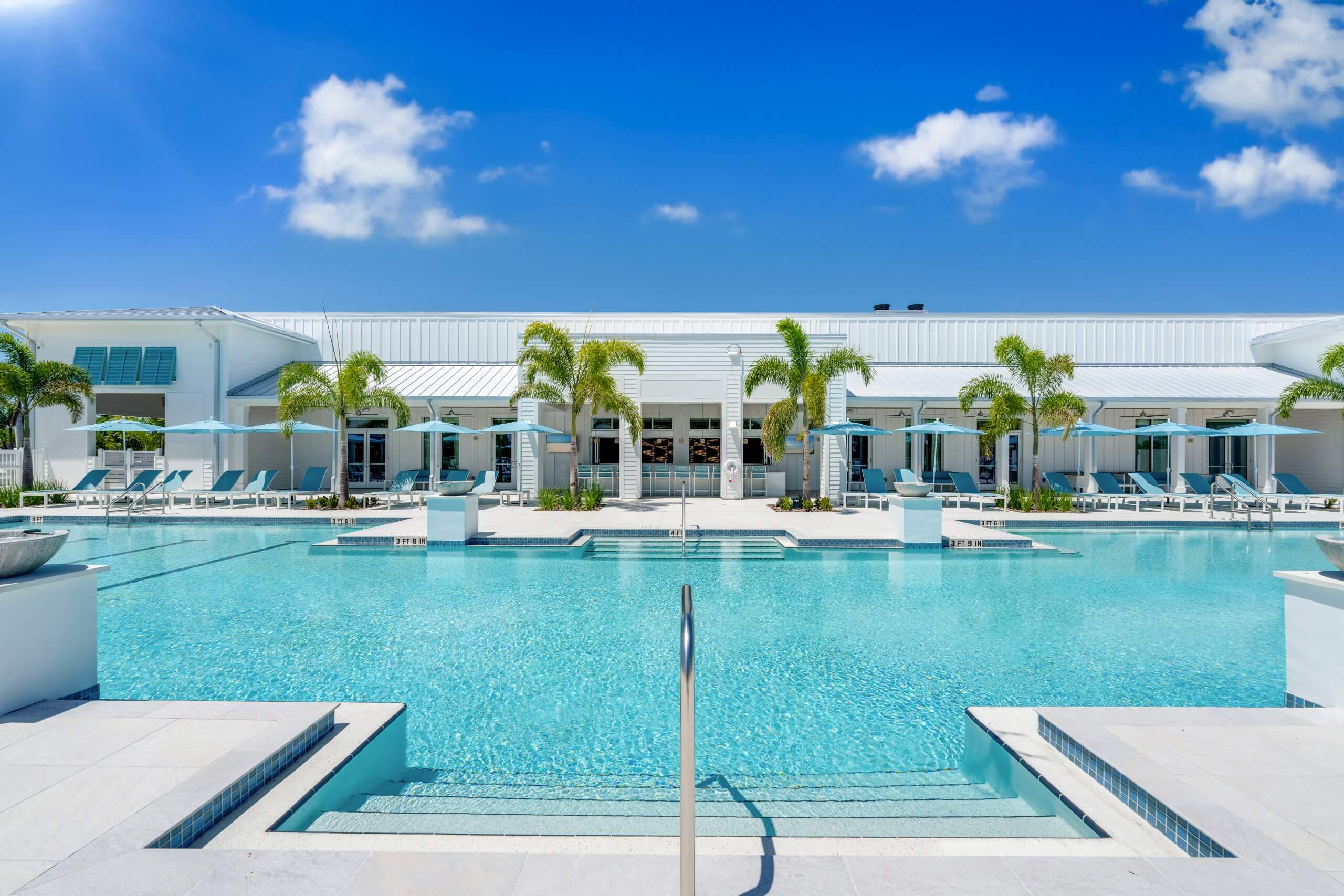 Front-facing view of a sparkling pool with steps leading in, surrounded by lounge chairs and palm trees in Bonita Springs, FL